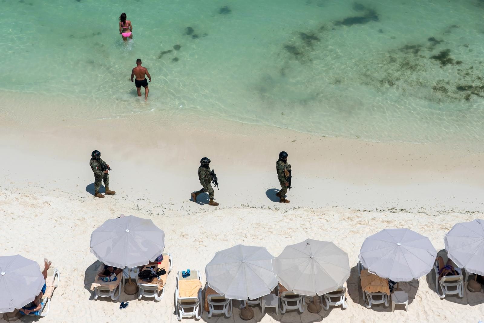 Soldados patrullando la orilla de una playa con sombrillas y bañistas