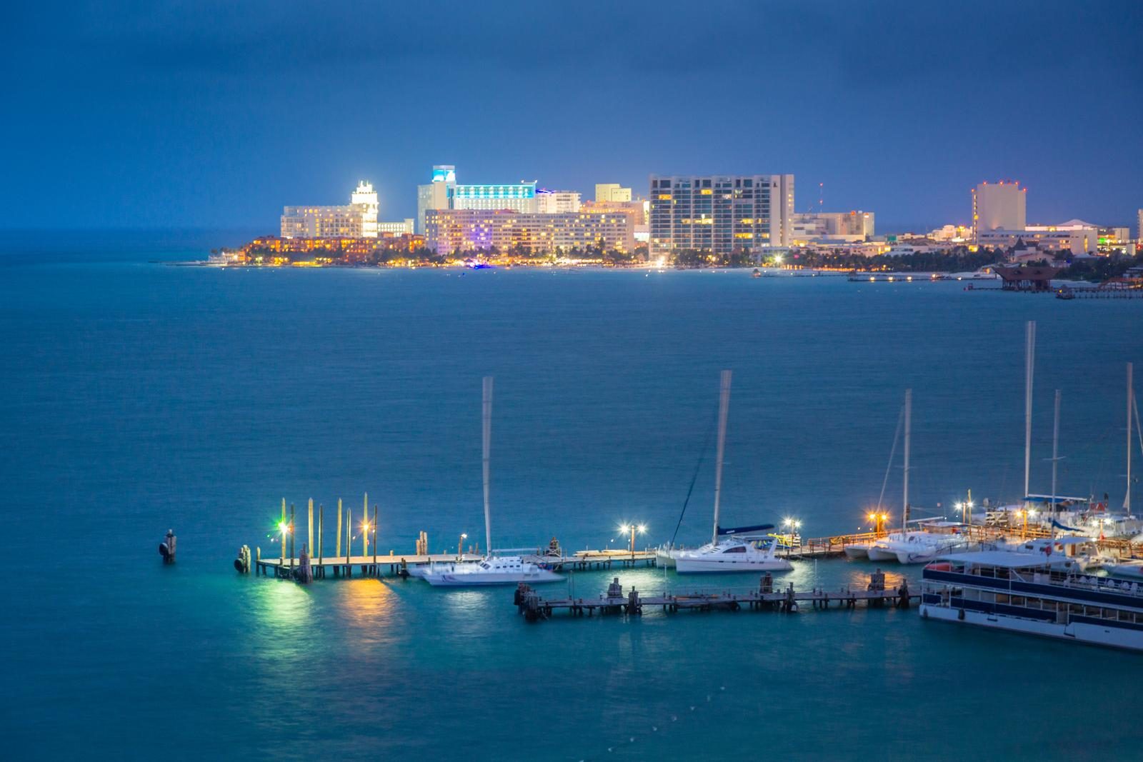 Muelle con veleros de noche frente a una zona hotelera iluminada
