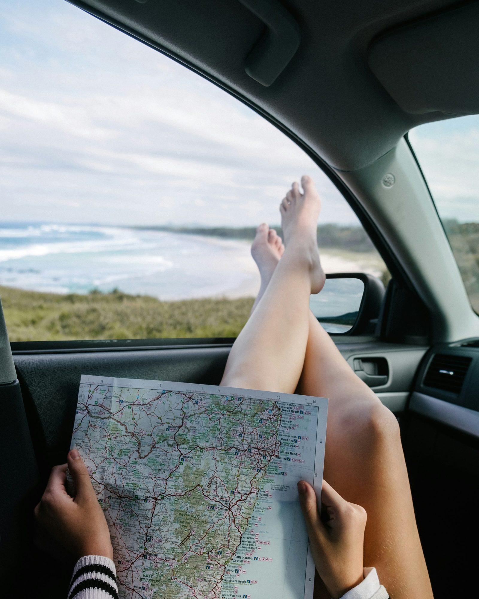 Viajera con los pies en la ventanilla de un auto mientras revisa un mapa de carreteras