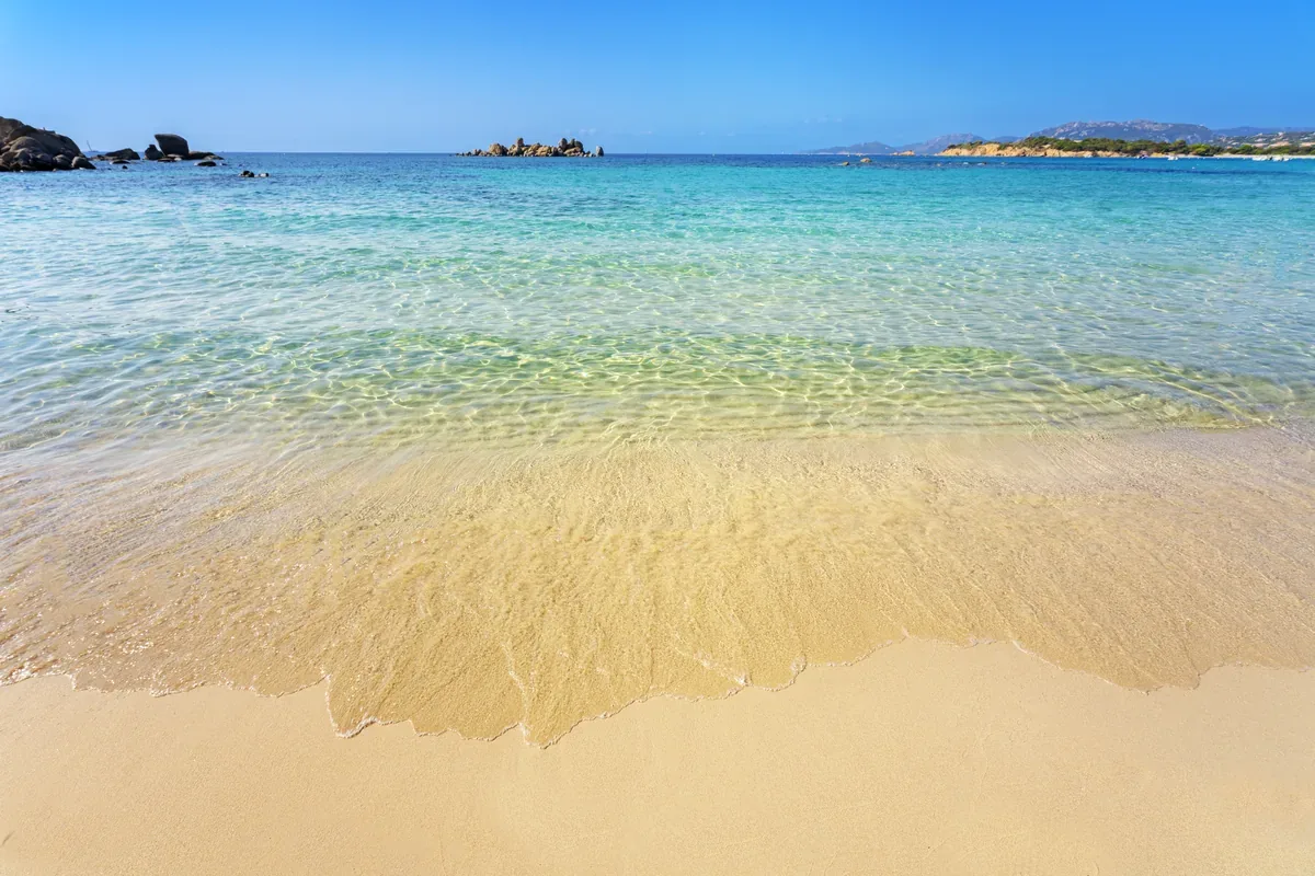 Playa de arena dorada y agua cristalina con islotes al fondo