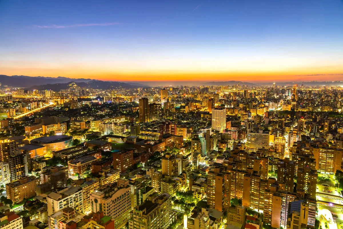 Panorámica de una ciudad iluminada al anochecer con montañas al fondo