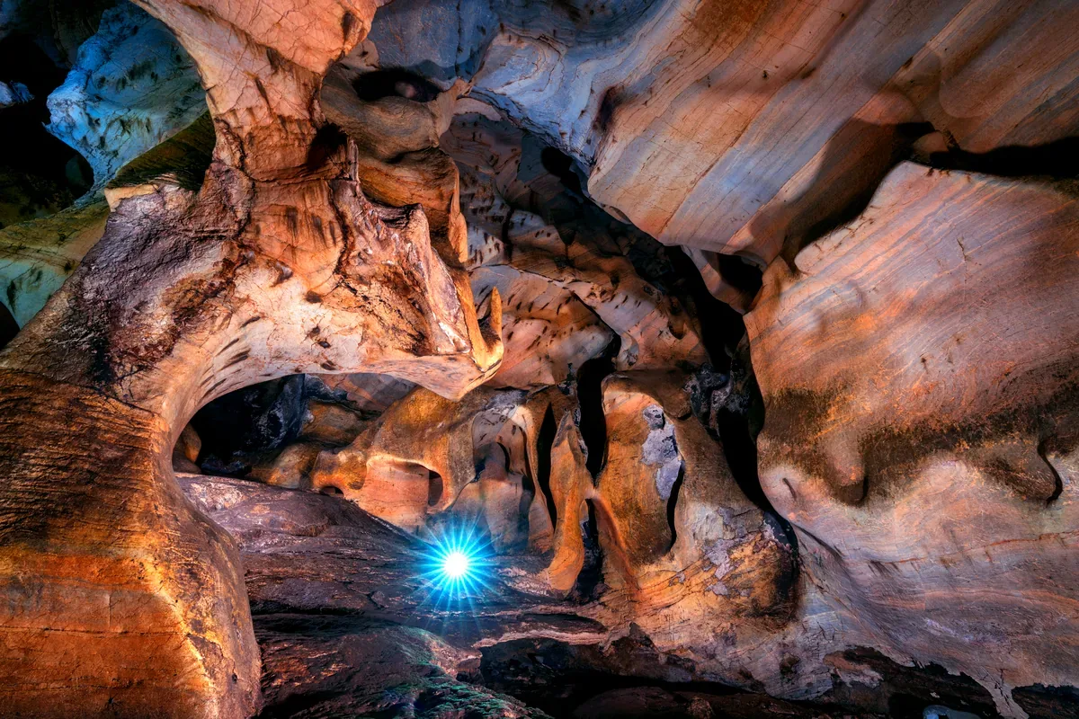 Cueva de roca rojiza y ocre con una luz azul al fondo