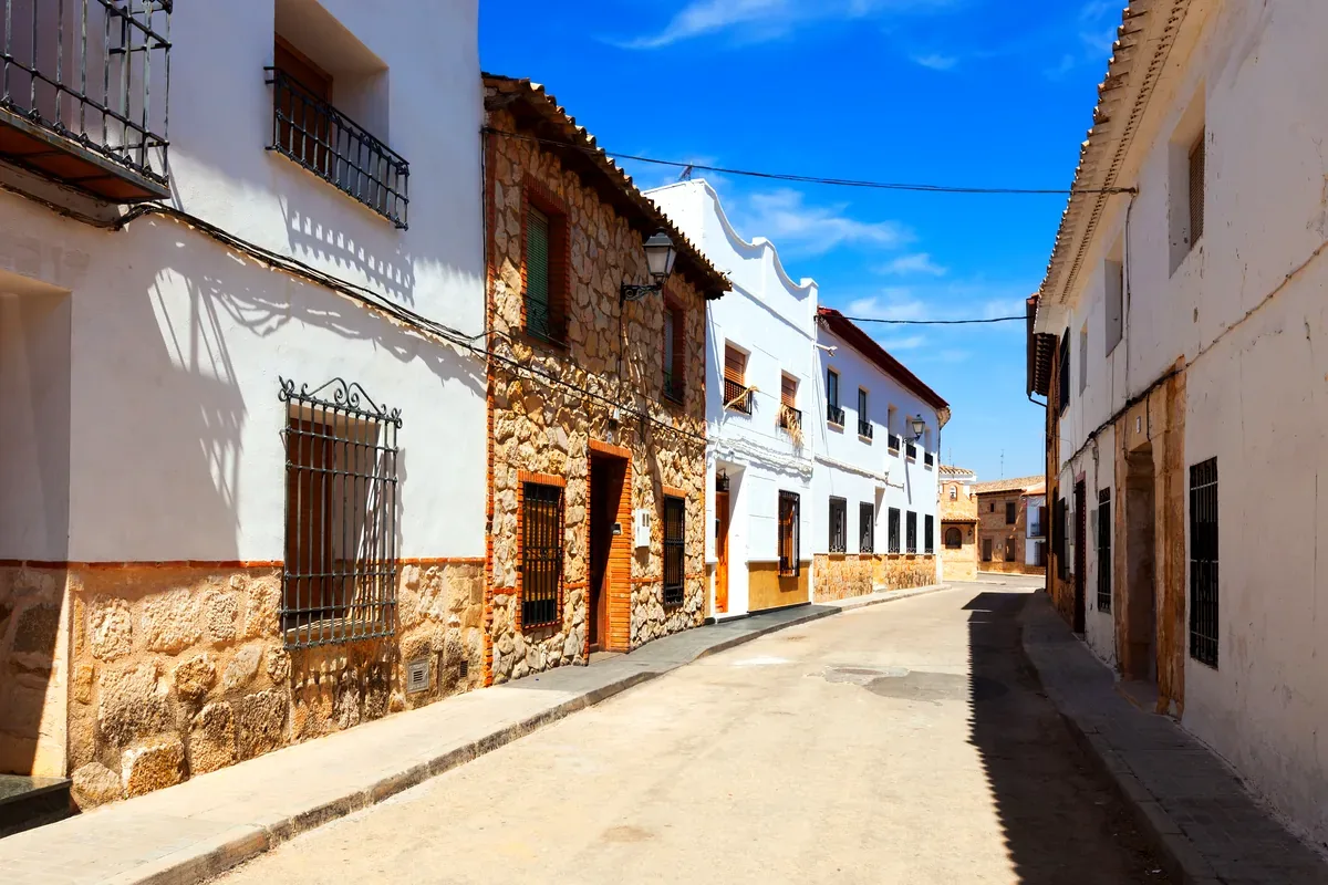 Calle de un pueblo con casas blancas y muros de piedra bajo un cielo azul