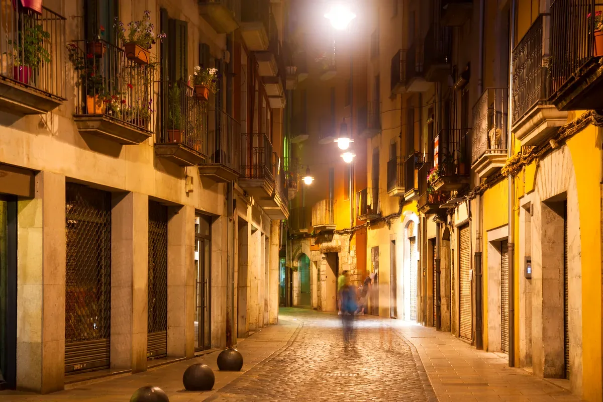 Calle angosta con faroles encendidos y balcones de noche