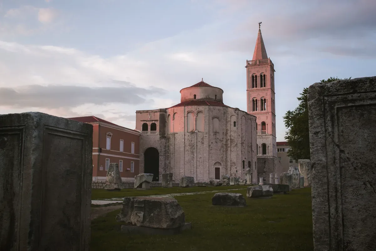 Iglesia circular de piedra y un campanario junto a ruinas antiguas al atardecer