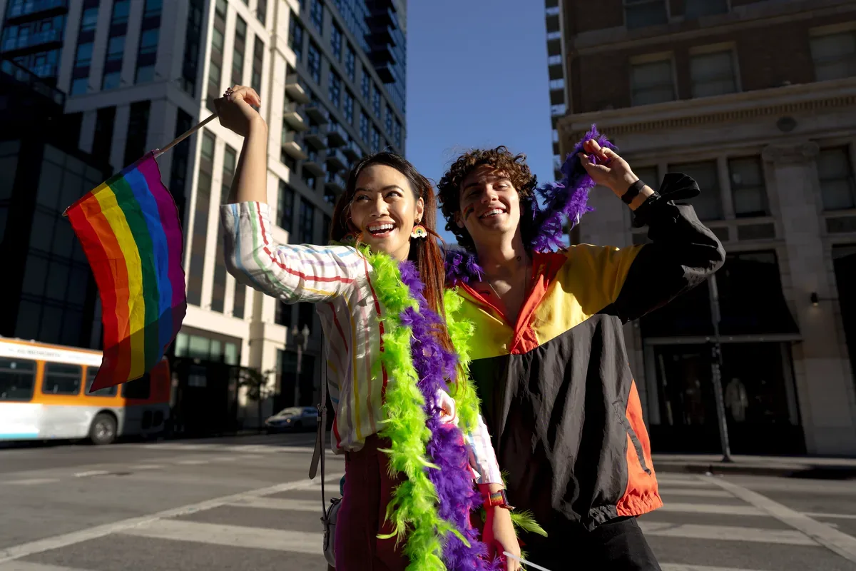 Pareja con una bandera de arcoíris y boas de plumas en una calle de la ciudad