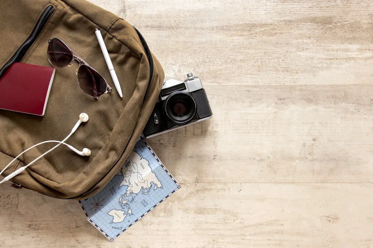 Mochila con pasaporte, lentes de sol, audífonos, cámara y mapa sobre una mesa