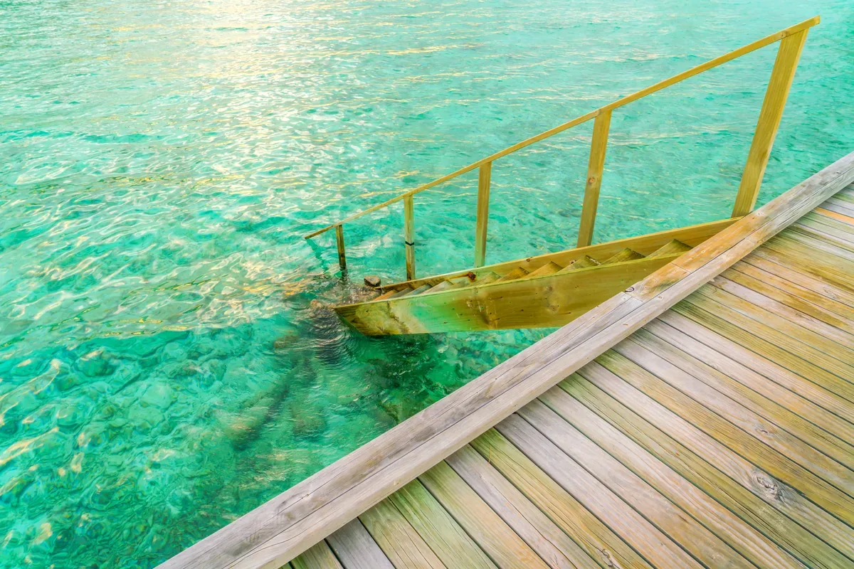 Escalera de un muelle de madera que baja a un agua verde turquesa