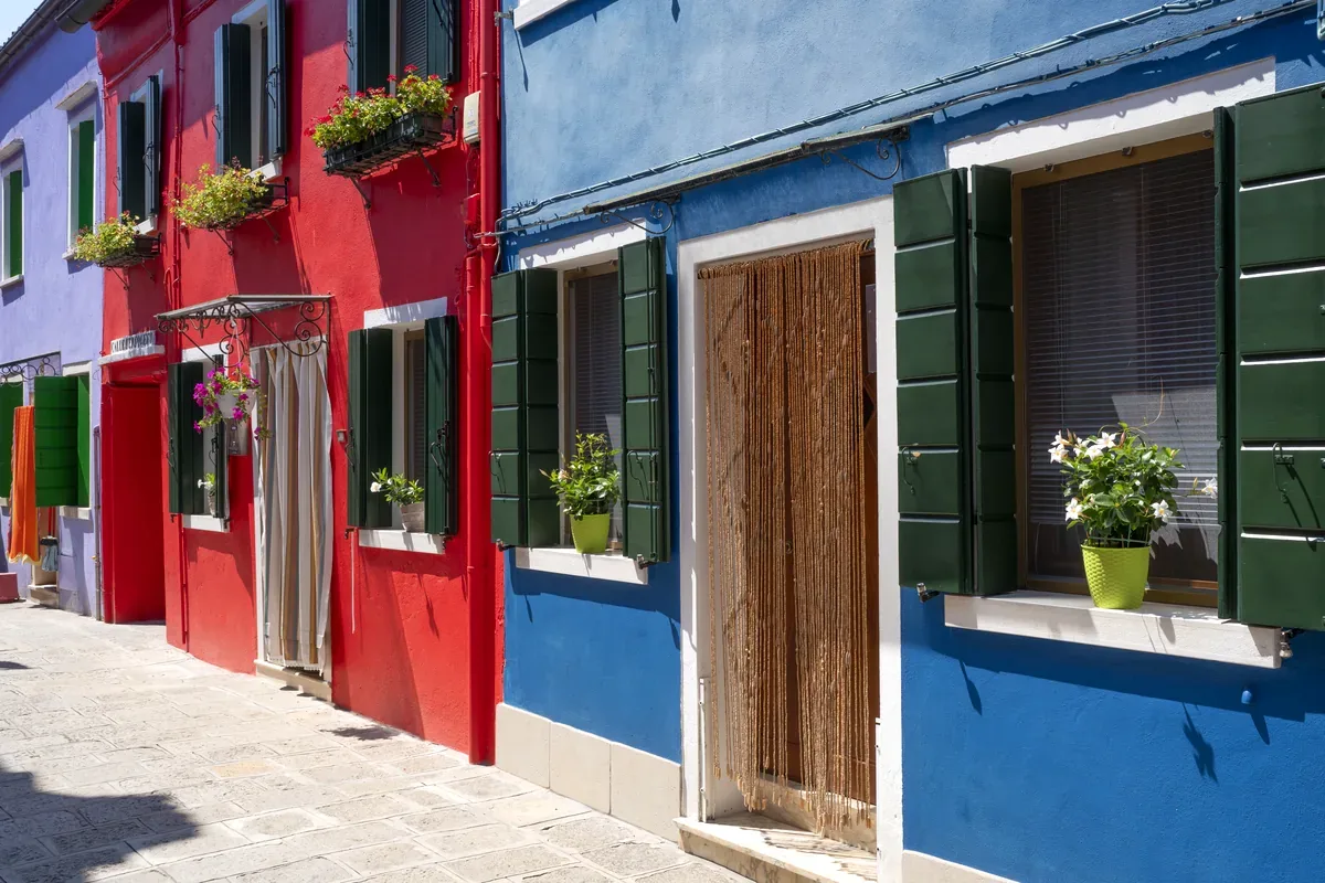 Calle con casas pintadas de rojo y azul con macetas en las ventanas