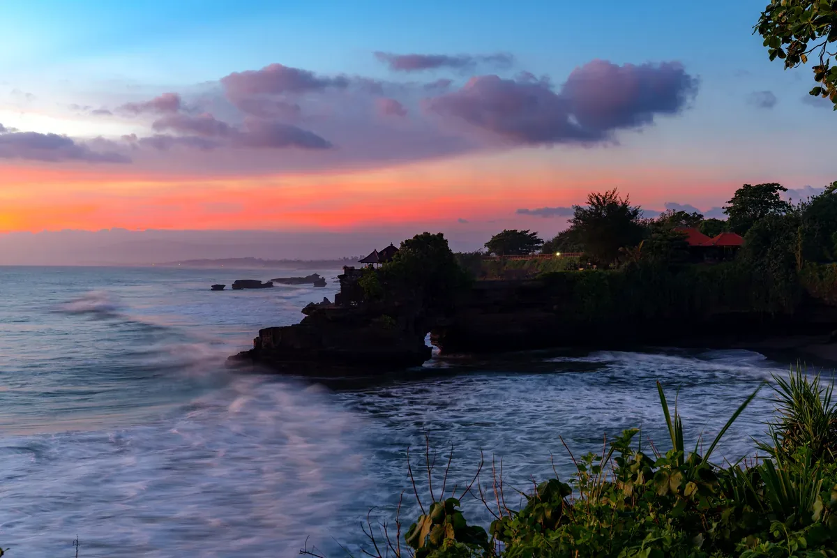 Atardecer rosado sobre un promontorio rocoso con vegetación junto al mar