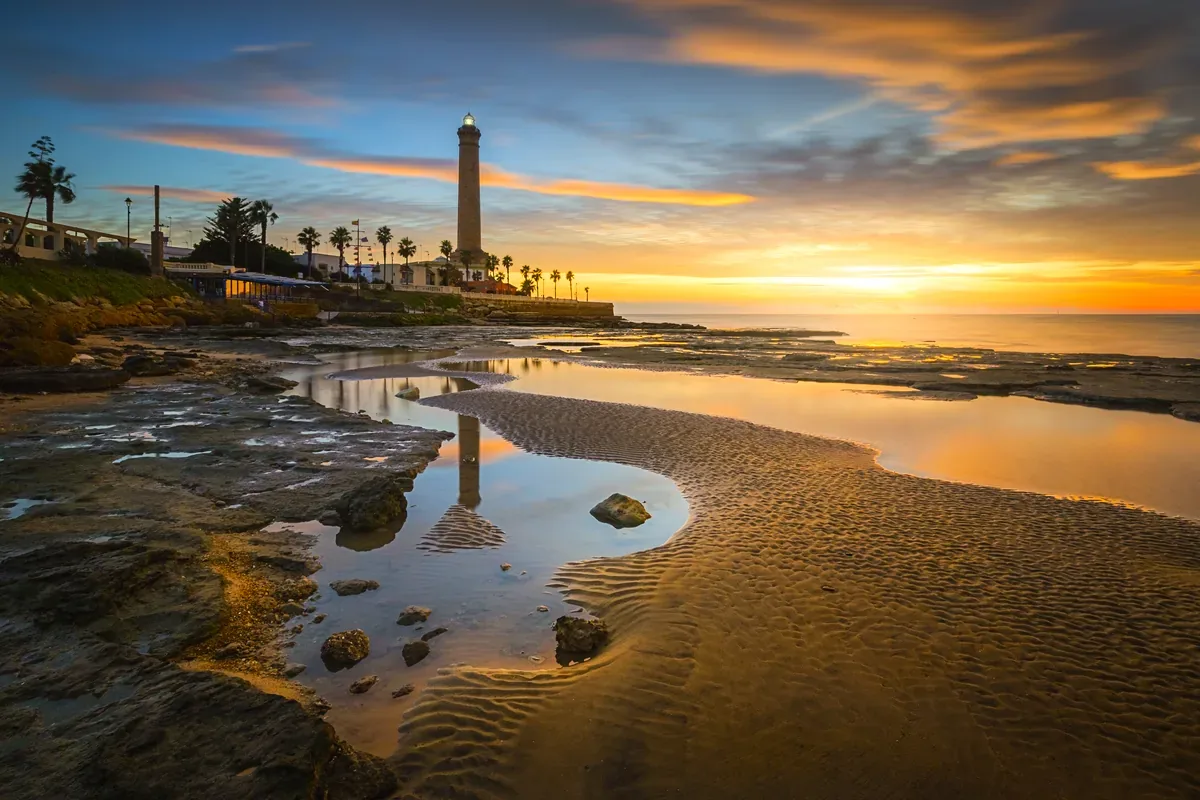 Faro junto a una costa rocosa con pozas al atardecer