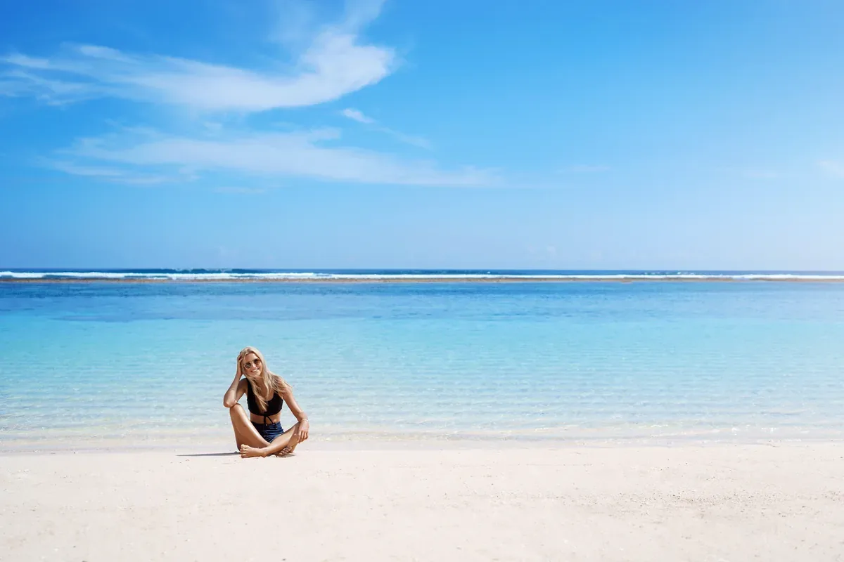 Mujer sentada en una playa de arena blanca con agua transparente