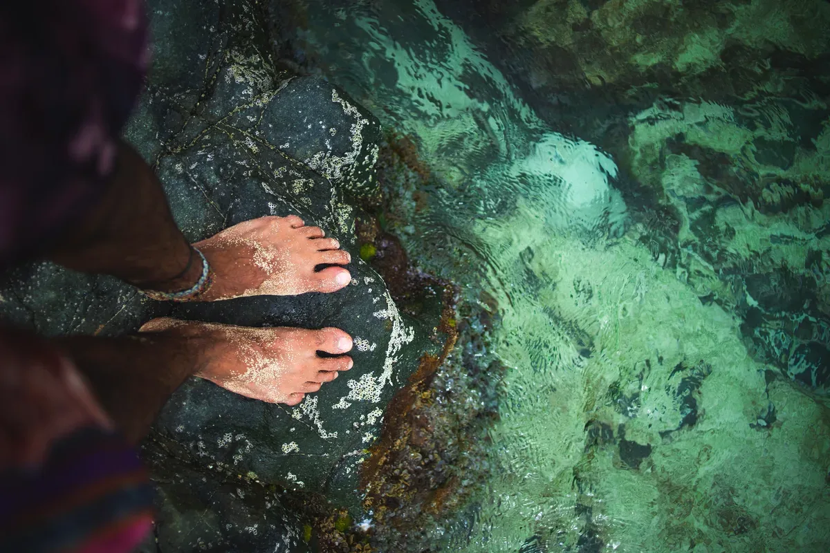 Pies sobre una roca dentro de un agua cristalina verde