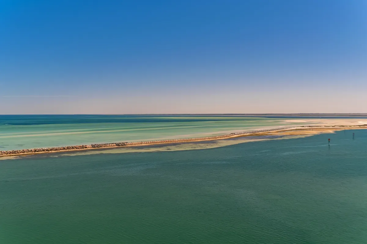 Mar verde en calma con una franja de arena al fondo al atardecer