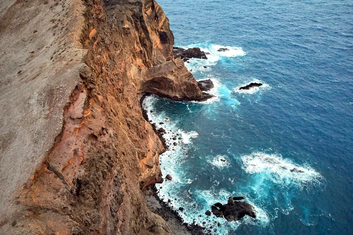 Vista aérea de un acantilado de roca rojiza junto al mar azul con olas