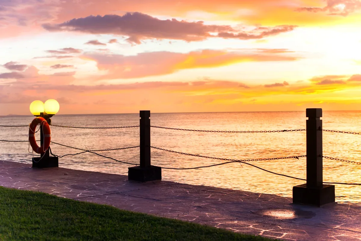 Malecón con faroles y un salvavidas frente al mar al atardecer