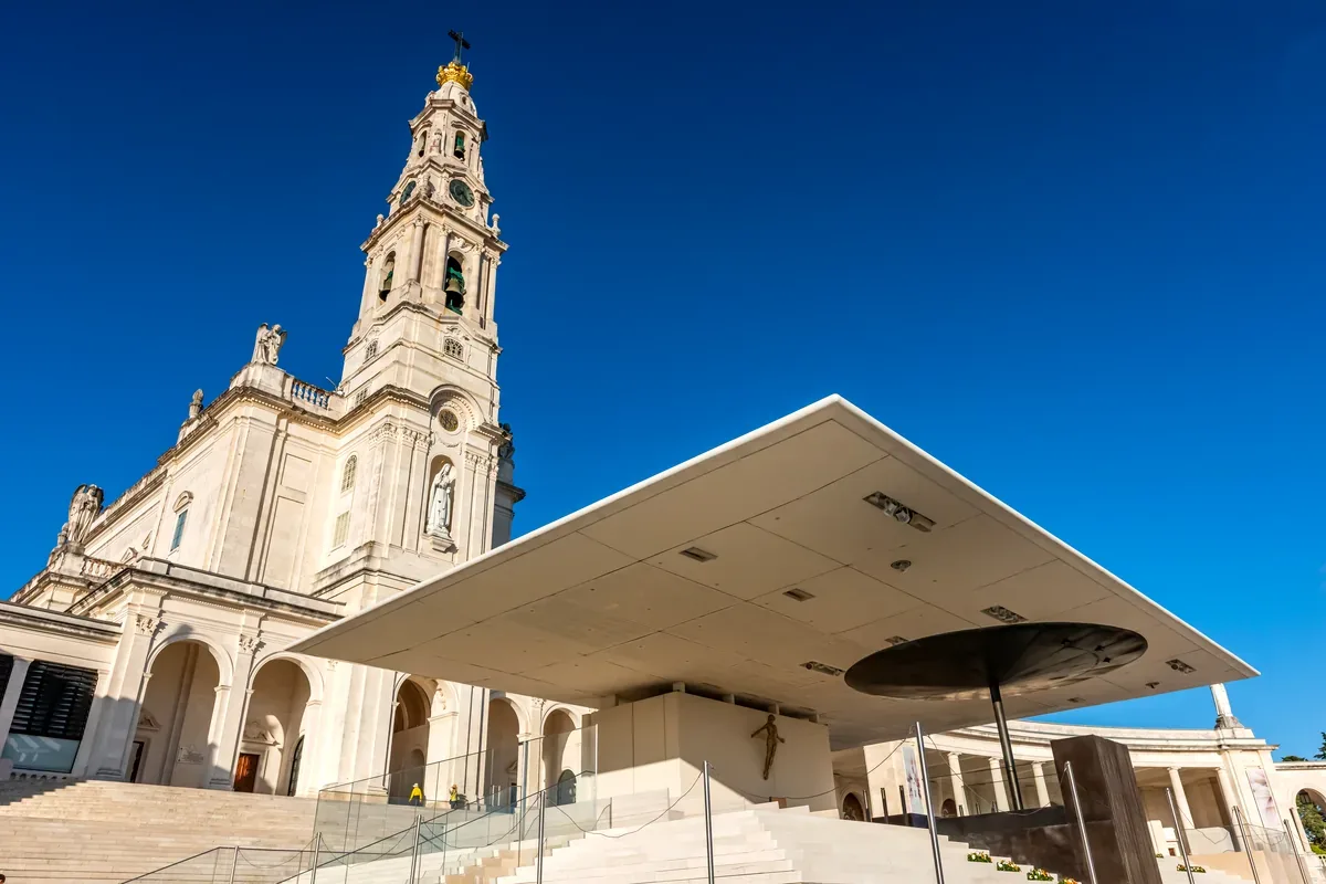 Basílica blanca con un campanario alto y una estructura moderna frente a ella