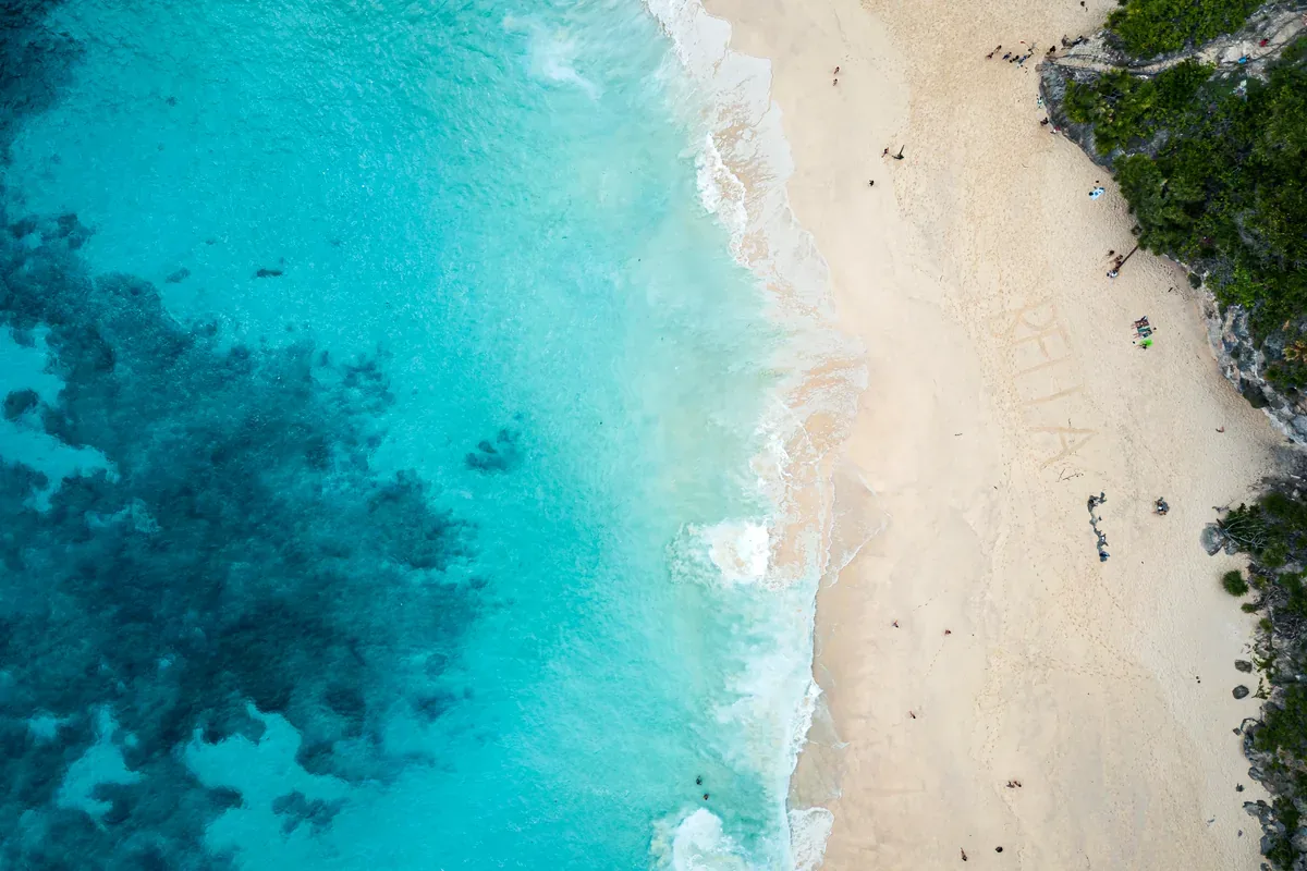 Vista aérea de una playa de arena blanca junto a un mar turquesa con arrecifes