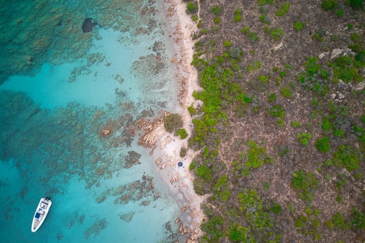 Lancha en una caleta de agua clara junto a una costa rocosa, vista desde el aire
