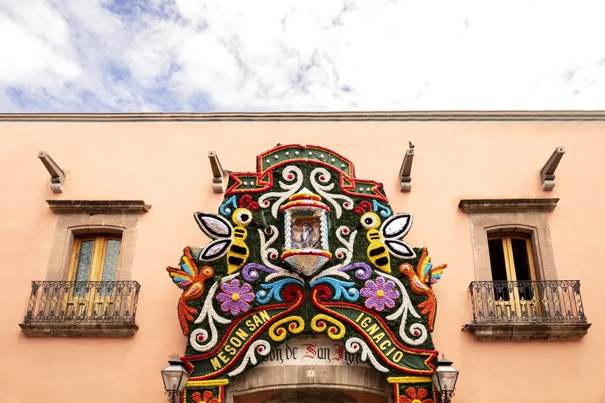Fachada rosa con una portada de colores decorada con flores y figuras sobre la entrada
