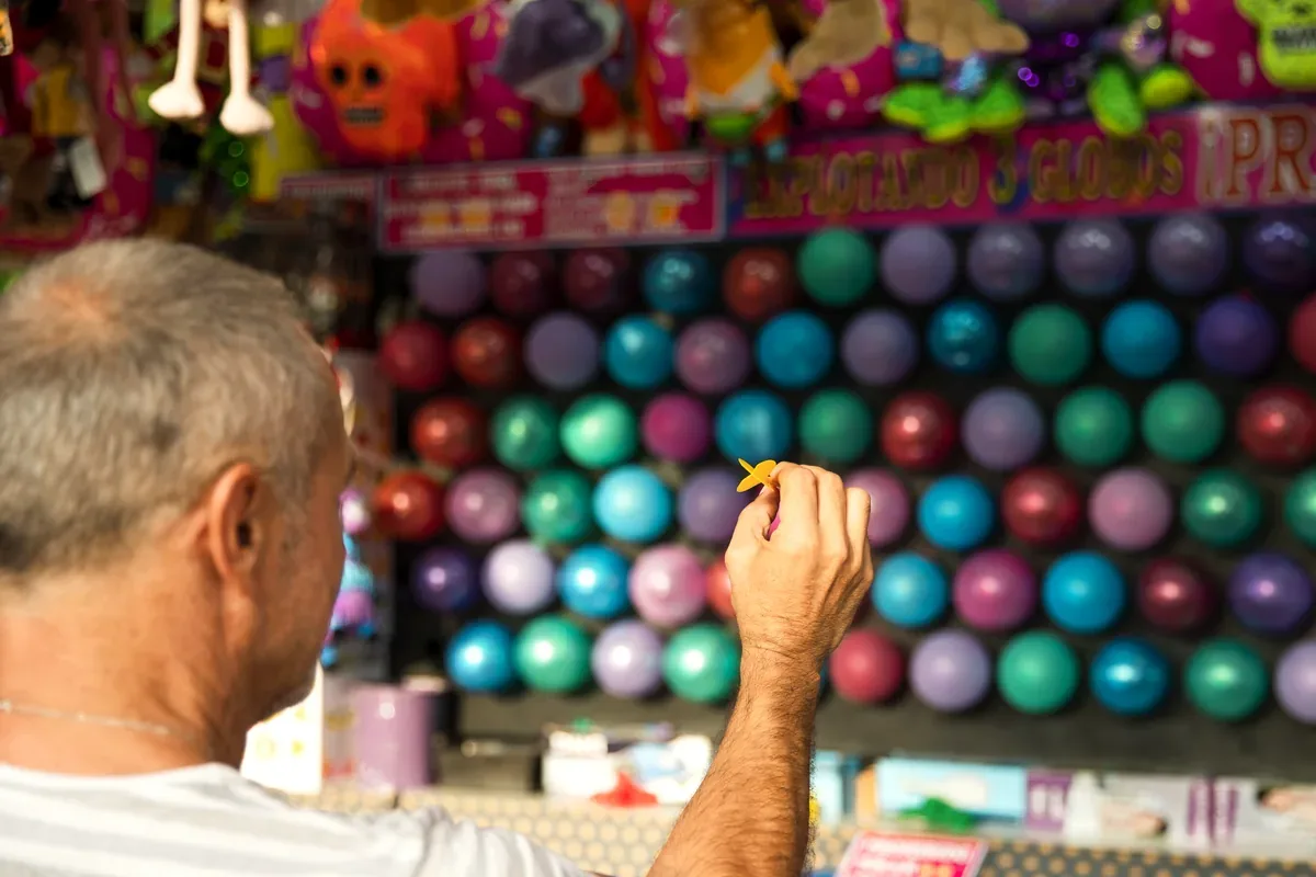 Hombre que lanza un dardo a globos de colores en un puesto de feria