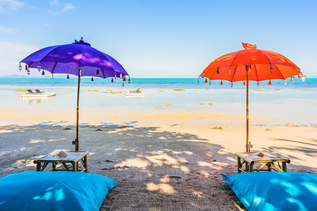 Sombrillas morada y naranja con cojines azules en una playa
