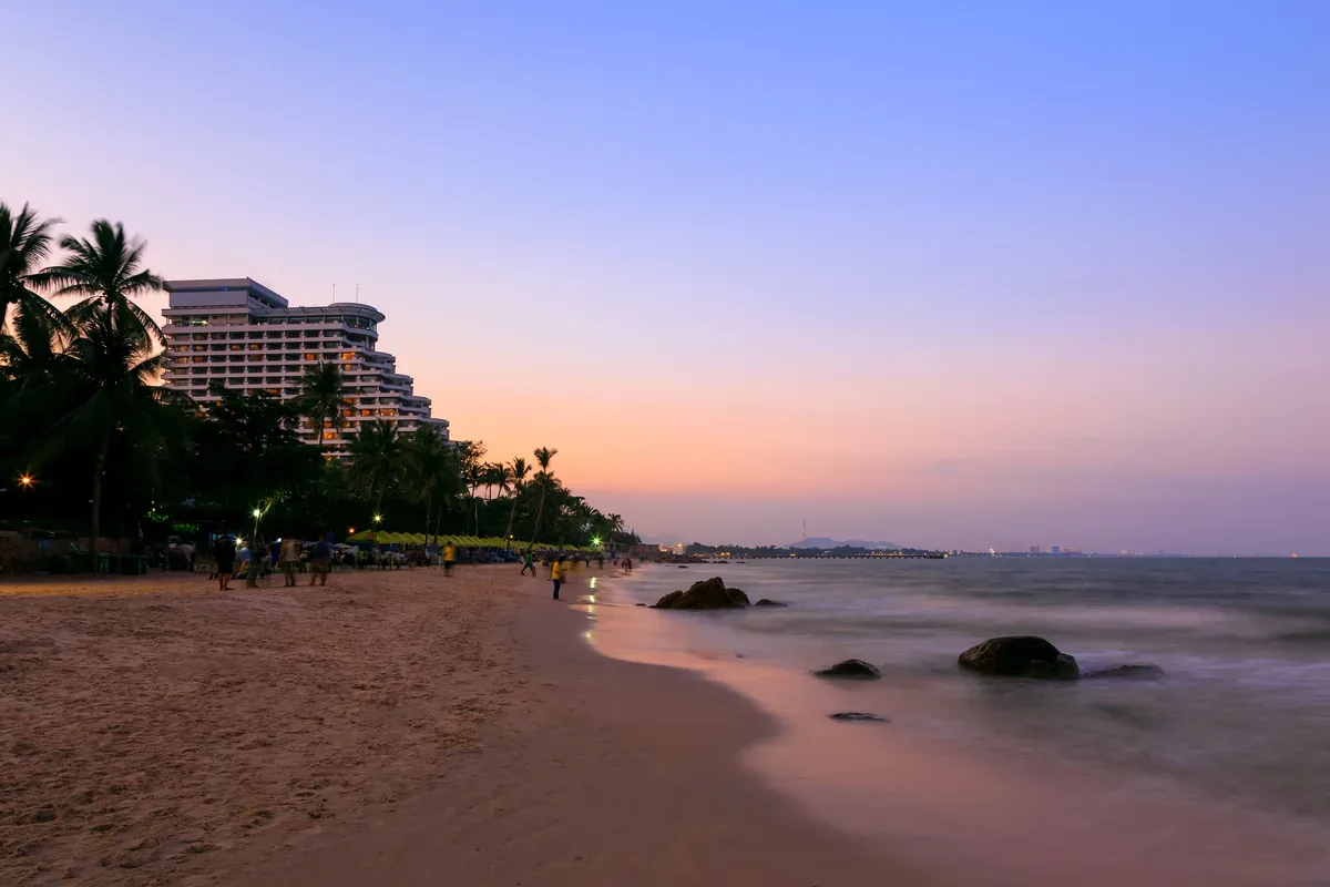Playa al anochecer con palmeras y un hotel al fondo