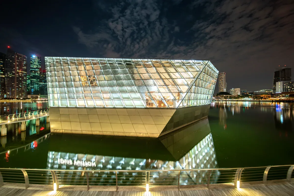 Edificio de cristal iluminado de noche reflejado en el agua de una bahía