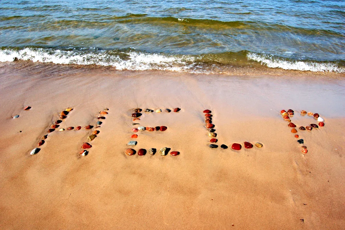 Piedras de colores que forman la palabra «help» en la arena de una playa