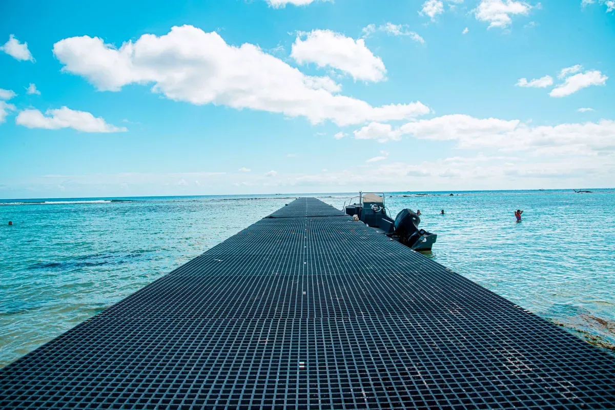 Muelle de rejilla que se adentra en el mar turquesa con una lancha a un lado