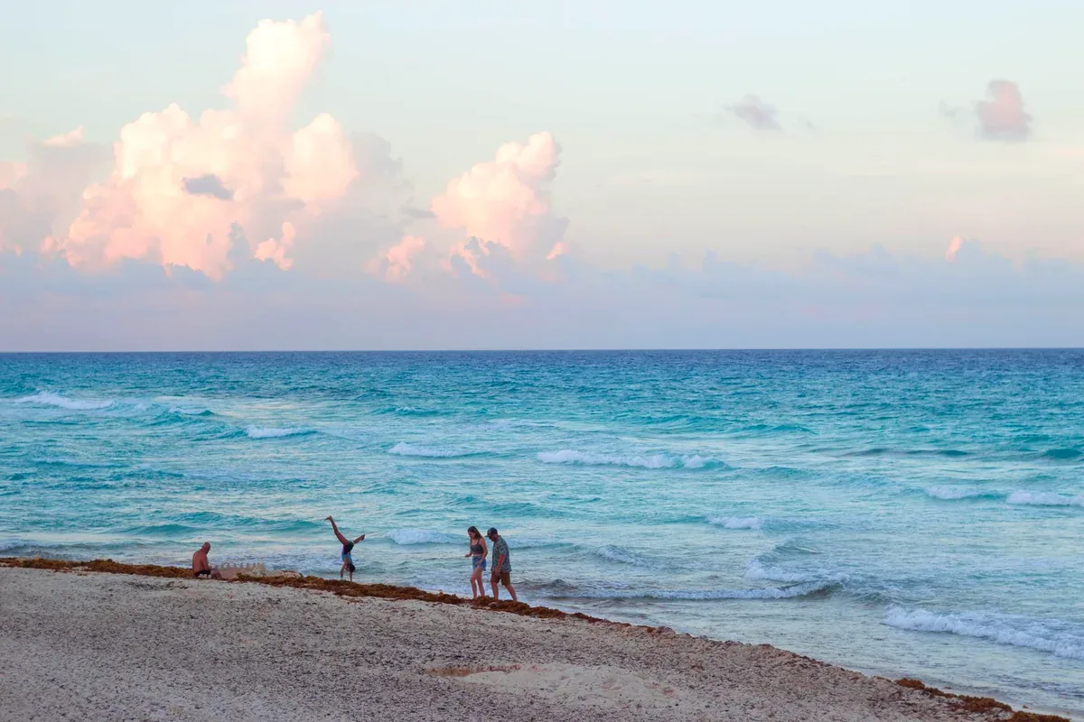 Mar turquesa con olas y personas en la orilla de una playa al atardecer