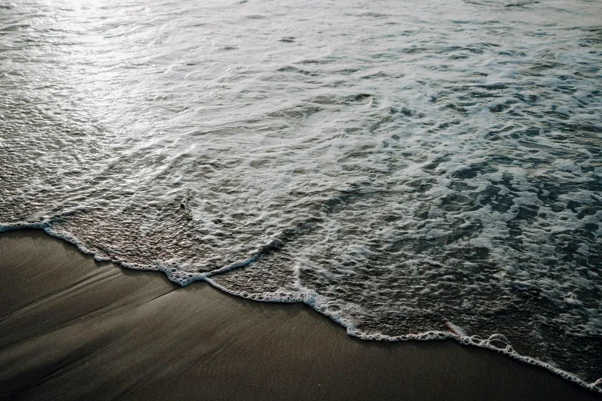 Ola que llega a la orilla de una playa de arena oscura