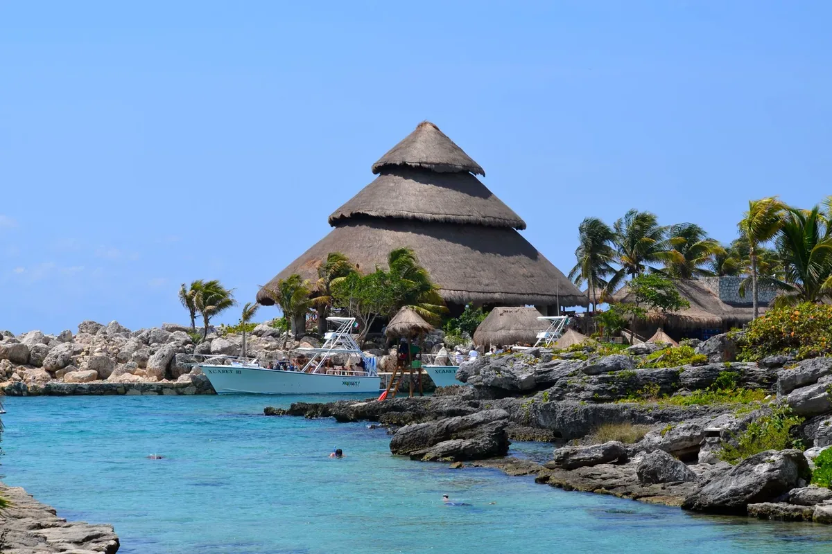 Palapa de varios niveles sobre una costa rocosa con agua turquesa y lanchas