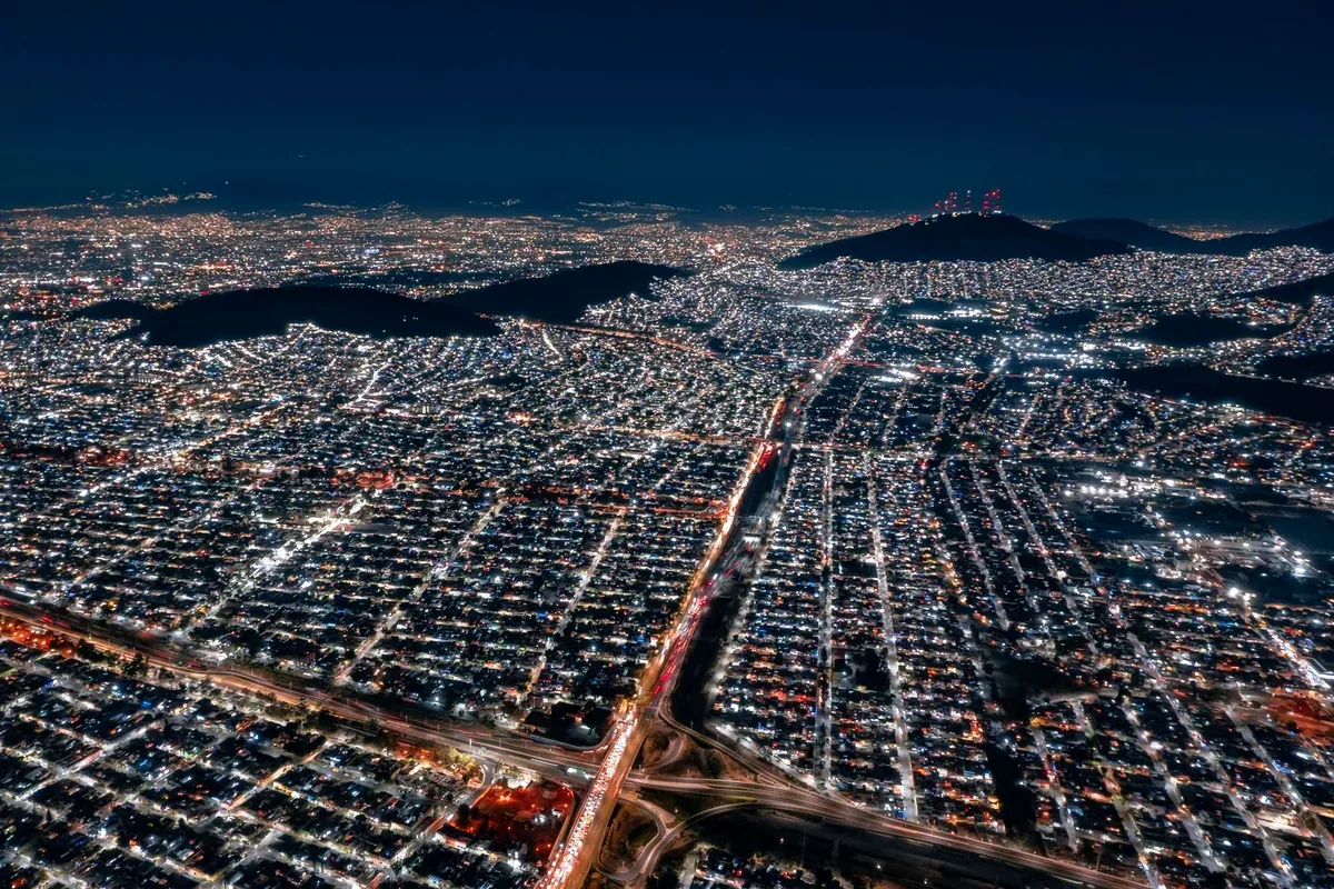 Vista aérea nocturna de una ciudad extensa con cerros al fondo