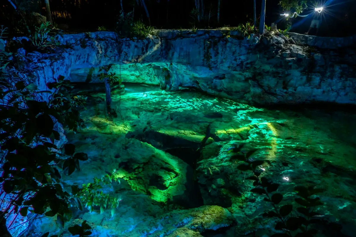 Cenote de agua verde iluminado dentro de una caverna