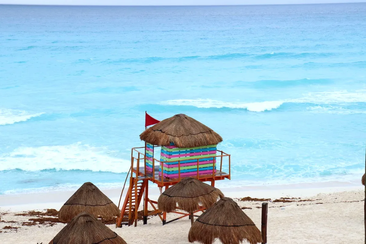 Caseta de salvavidas de colores y palapas en una playa de mar turquesa