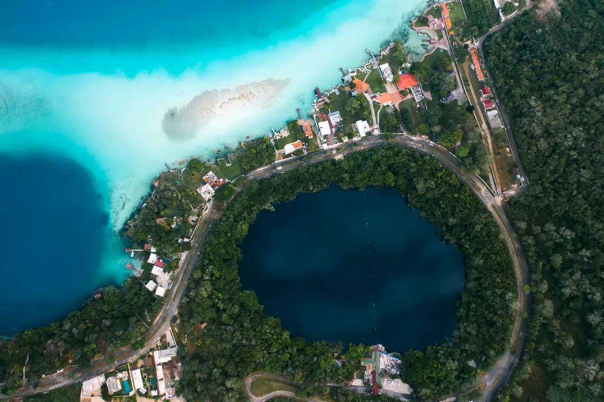Vista aérea de un cenote circular de agua azul oscuro junto a una laguna turquesa