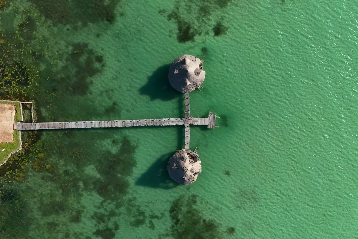 Vista cenital de un muelle con dos palapas en agua verde