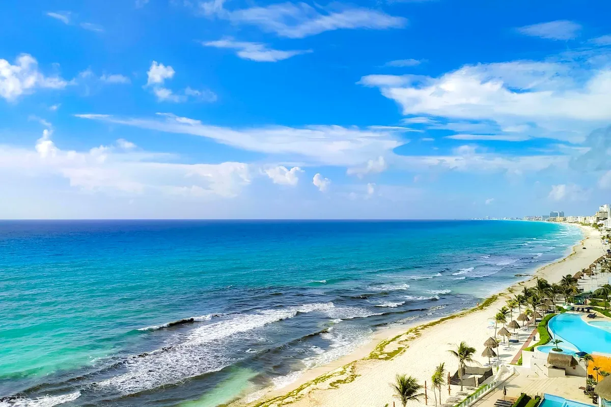 Costa con olas, albercas de hoteles y una playa de arena blanca bajo un cielo azul