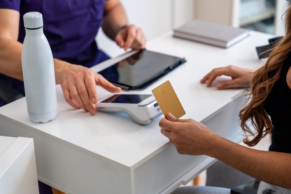 Persona que acerca una tarjeta a una terminal de pago sobre un escritorio