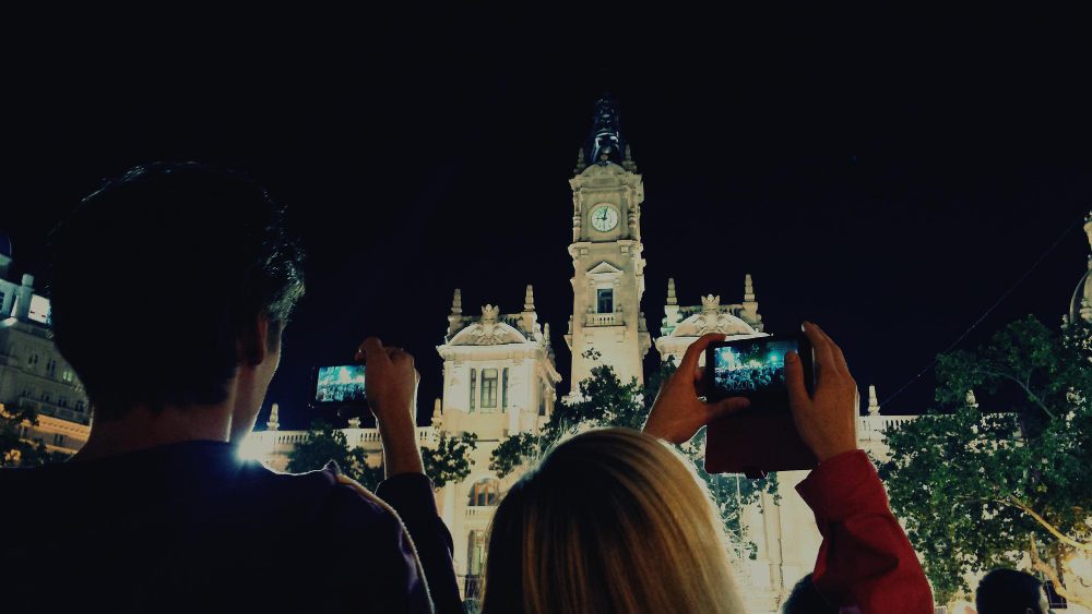 Personas que toman fotos de noche a un edificio iluminado con torre de reloj