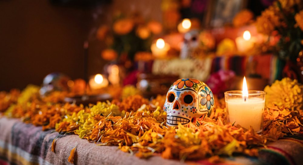 Calavera de azúcar y velas sobre una ofrenda cubierta de pétalos de cempasúchil