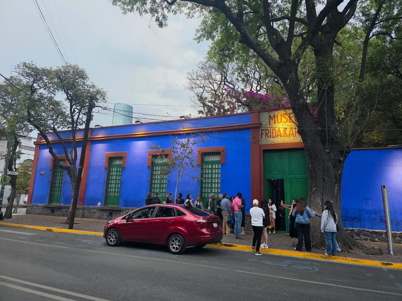 Fachada azul de la Casa Azul, el Museo Frida Kahlo, con visitantes haciendo fila junto a la puerta verde