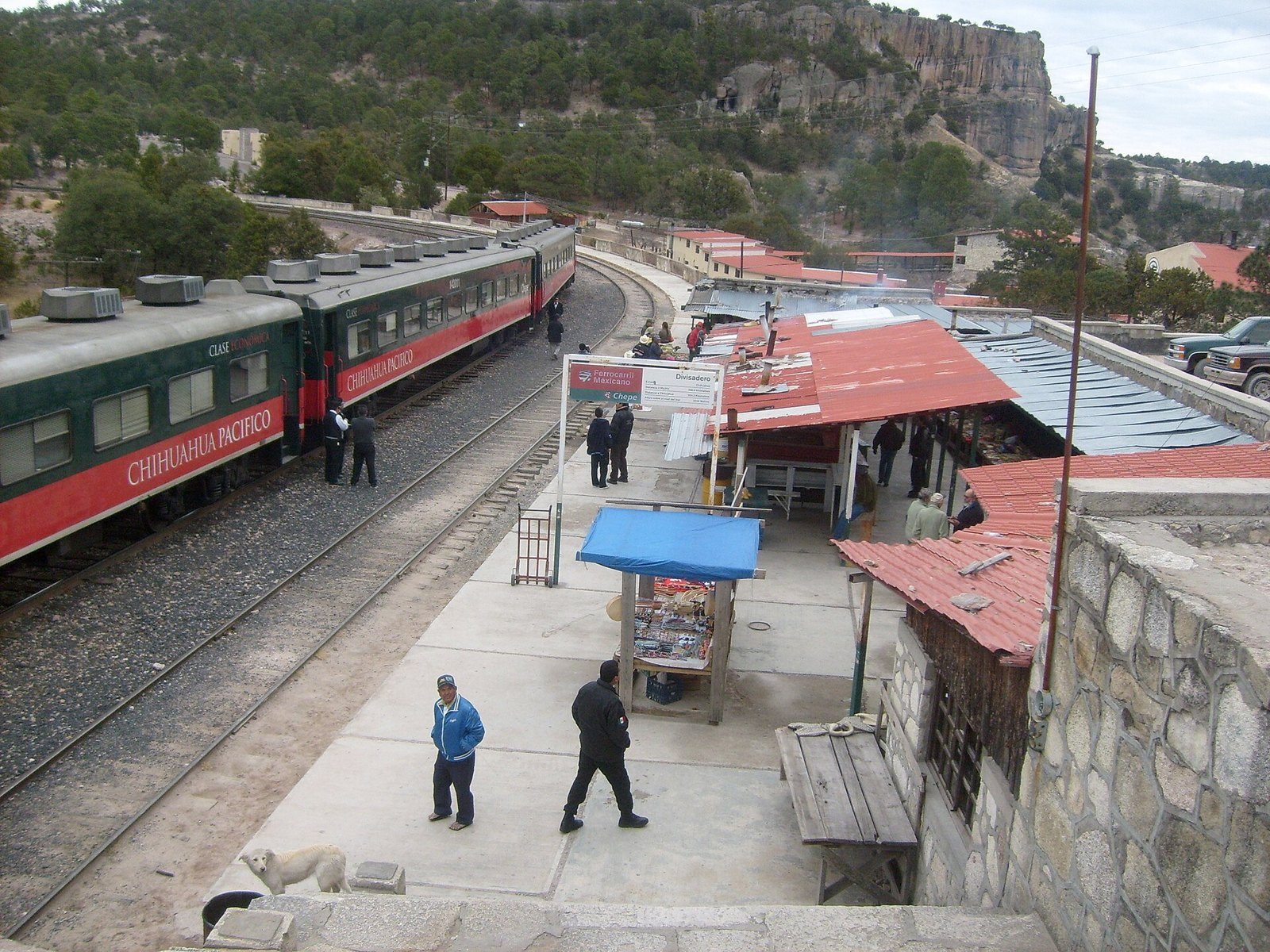 Tren de pasajeros junto al andén de la estación de Divisadero, con las barrancas y edificios de techo de lámina al fondo