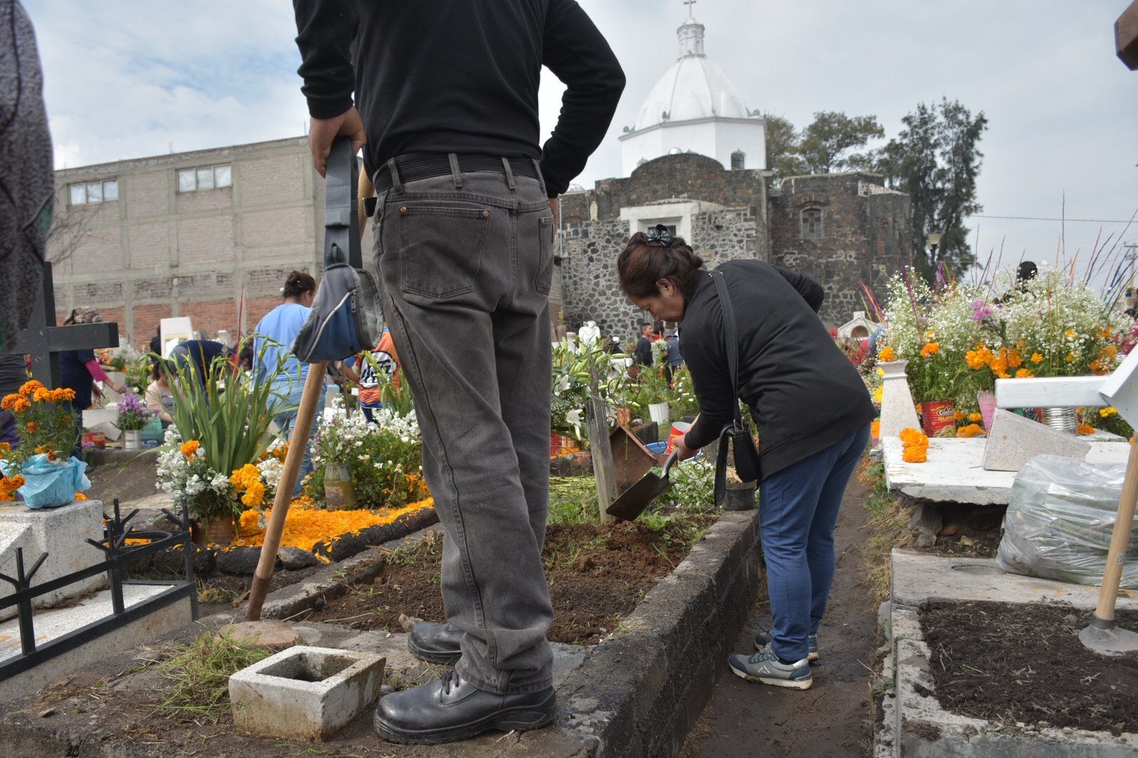 Familias arreglando tumbas con flores en el panteón de Mixquic