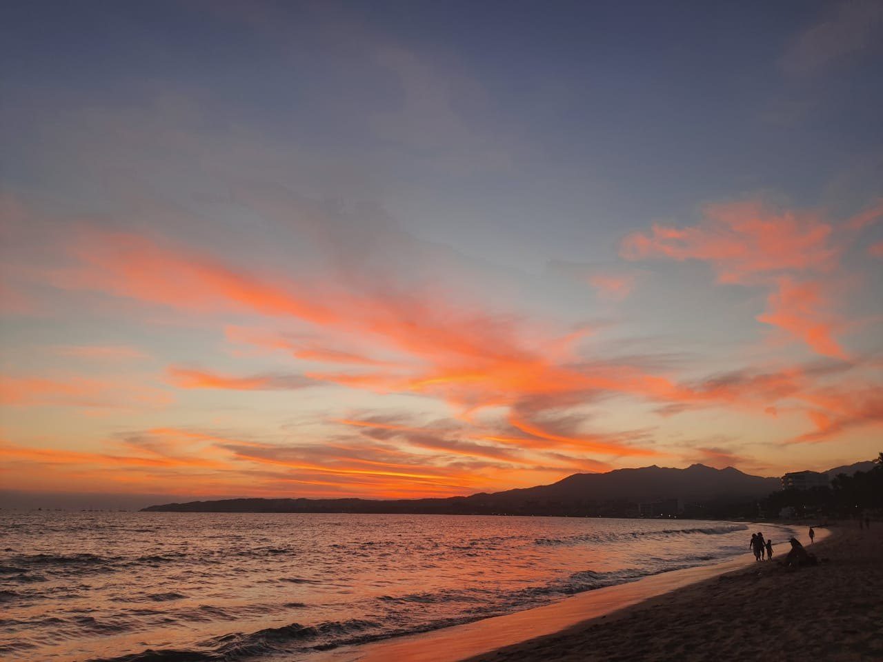 Atardecer en la playa de Punta de Mita con cielo anaranjado, el mar en calma y la silueta de los cerros al fondo