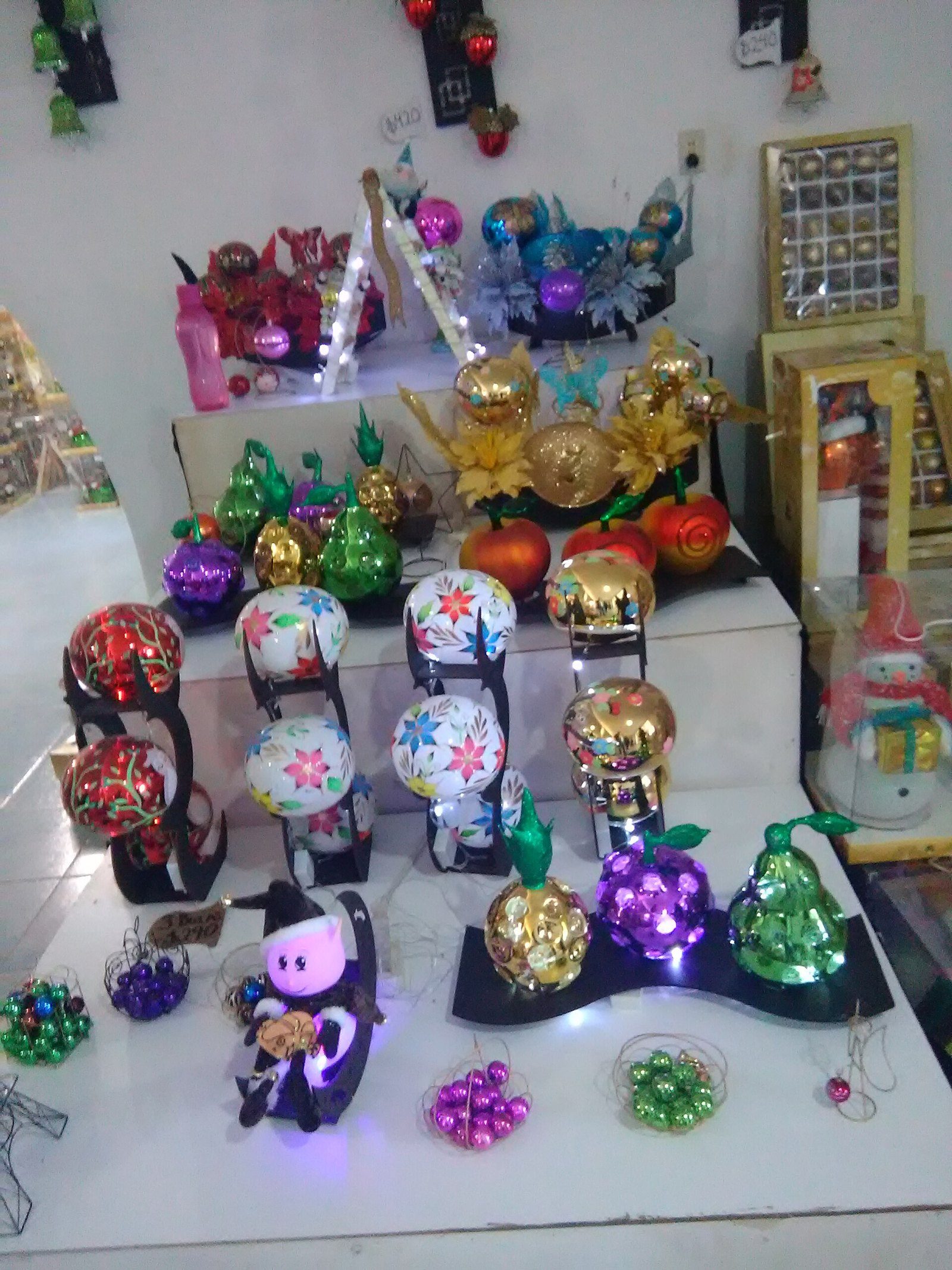 Esferas navideñas pintadas a mano con flores y adornos en forma de fruta, exhibidas en una tienda de Chignahuapan