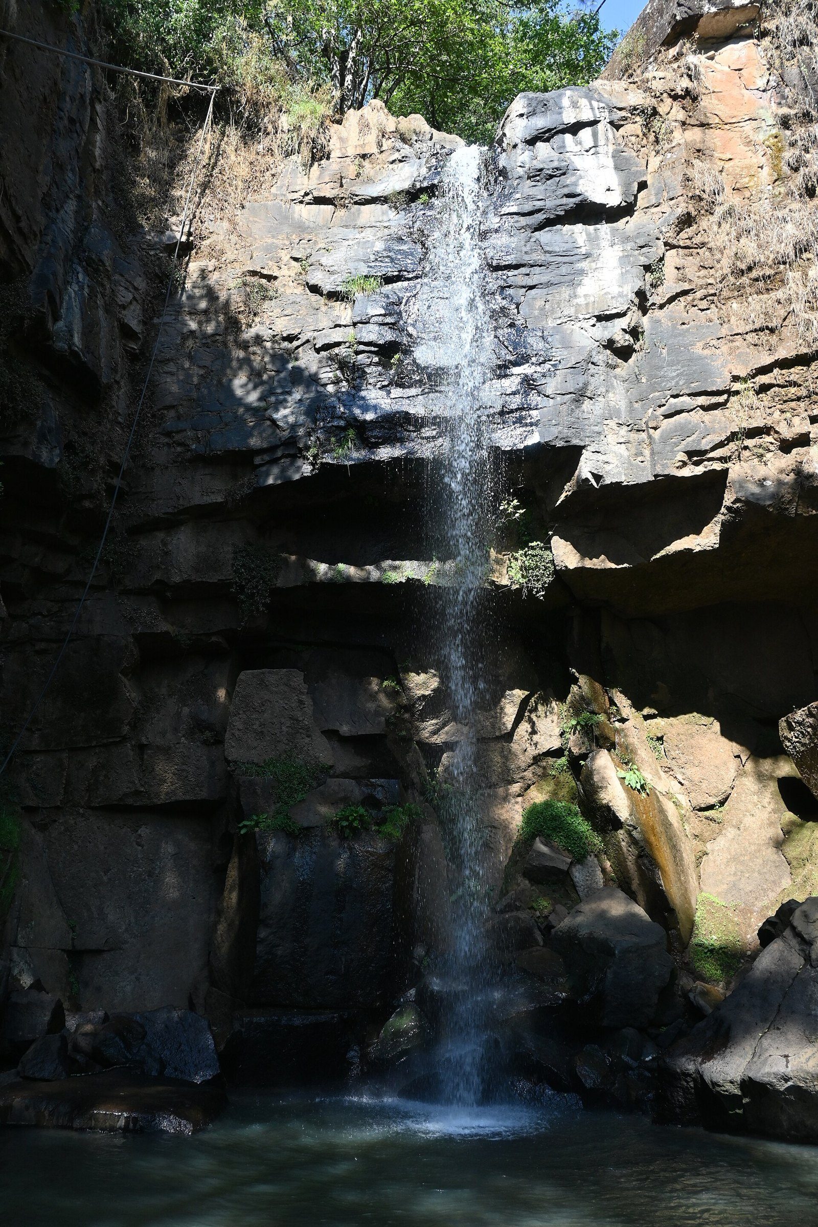 Cascada El Salto cayendo por una pared de roca oscura hacia una poza, rodeada de vegetación