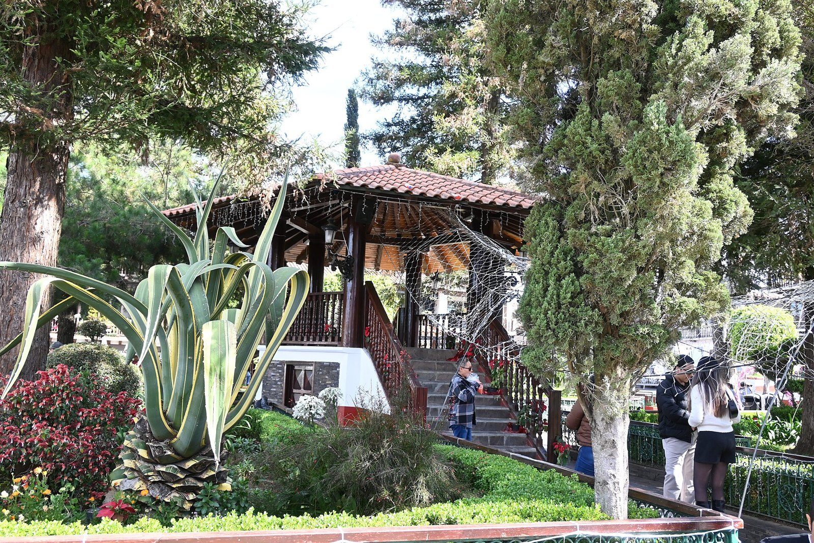 Quiosco de madera con techo de teja entre jardines y árboles en la plaza principal de Mazamitla
