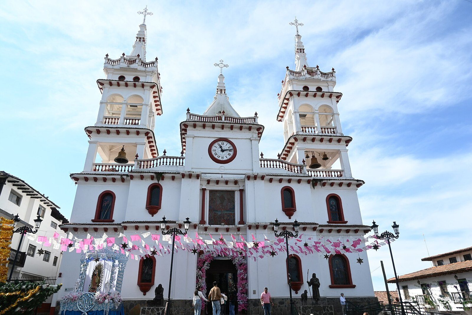 Fachada blanca con detalles rojos y dos torres de la parroquia de San Cristóbal en Mazamitla, con banderines de colores frente al templo